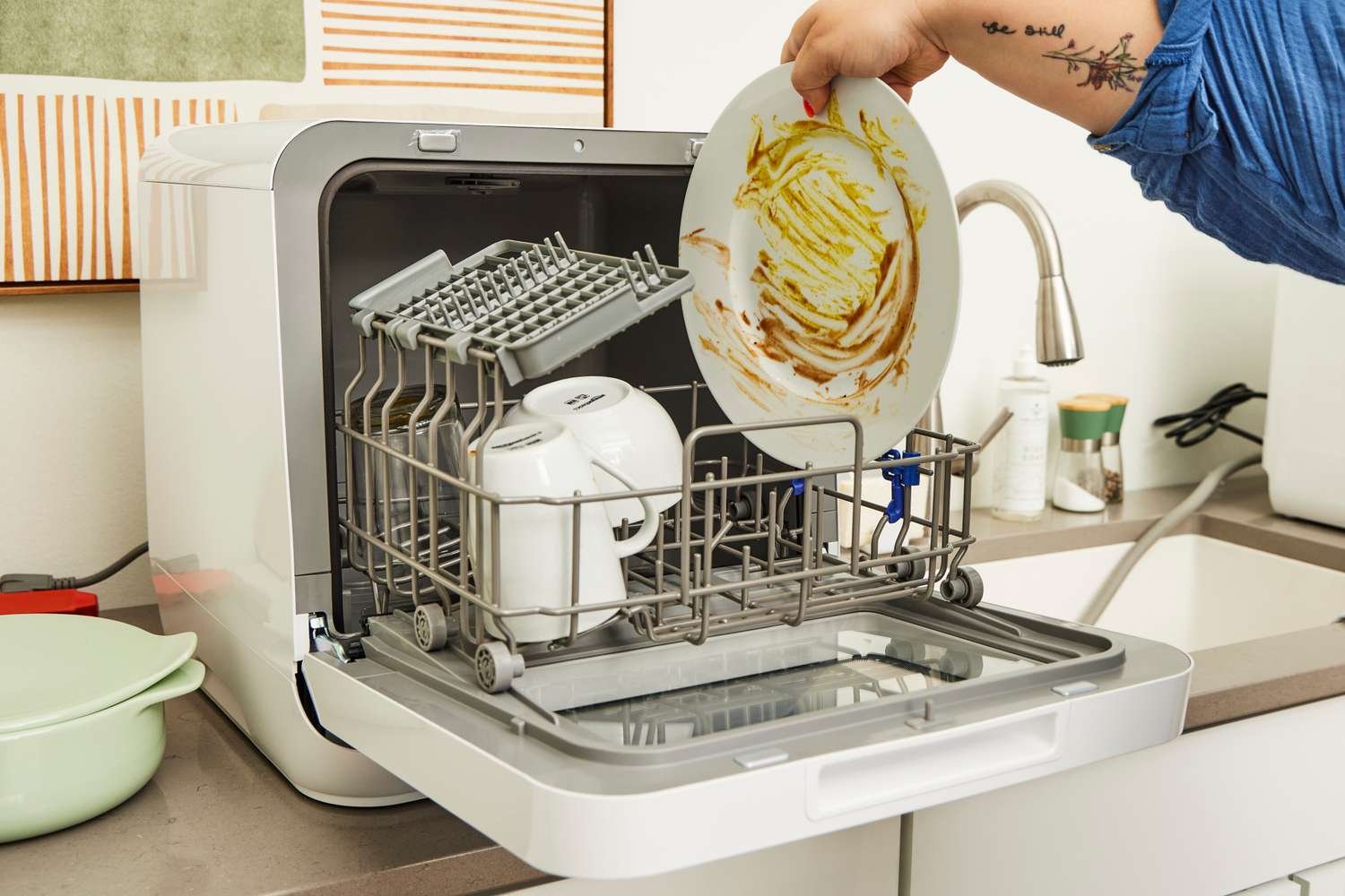 A compact countertop dishwasher sits on a marble kitchen counter in a modern home.